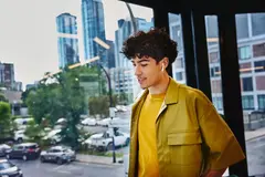 Male in yellow shirt, width earphones, standing at a window looking down