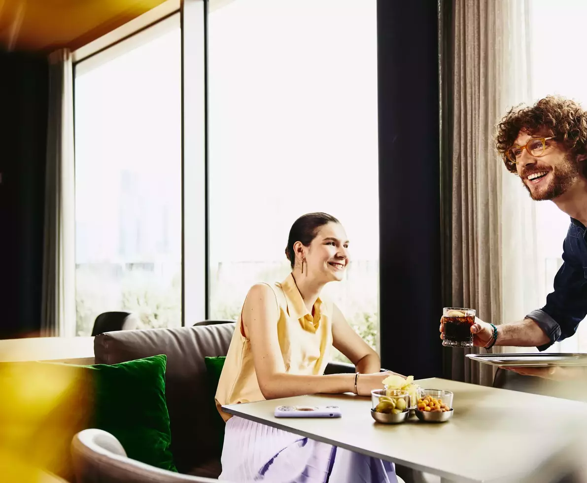 Waiter serving a drink to female sitting at a table.
