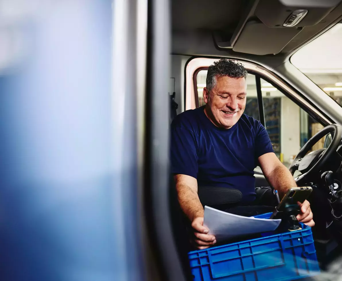 Smiling male sitting in driver's seat of a logistics truck holding papers and a GPS
