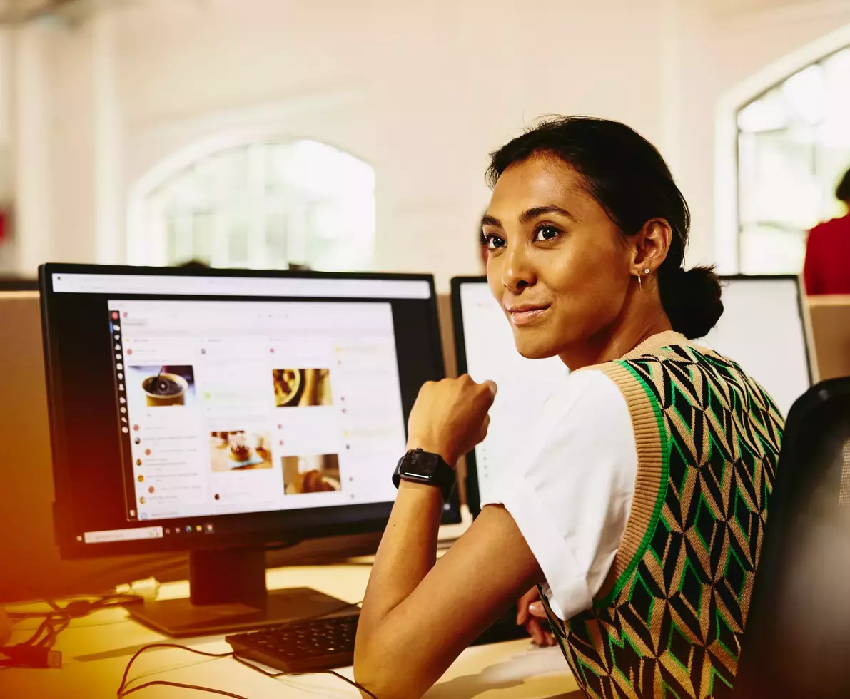 Womale sitting at her desk, looking away from computer screens displaying marketing content.
