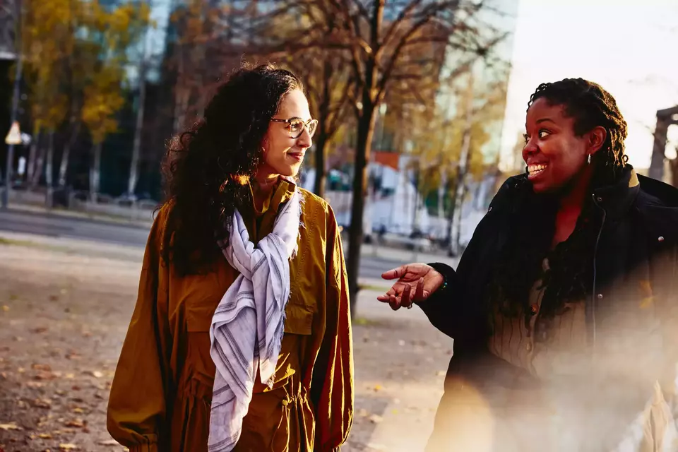 Two female walking outside while having a conversation, smiling.
