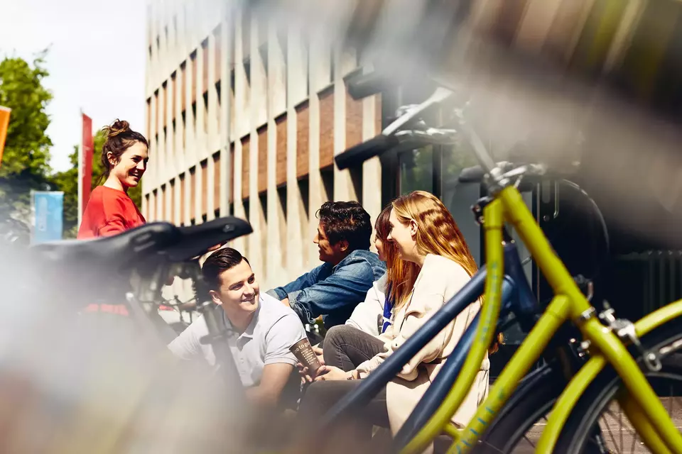 Group of students sitting outside next to bikes.
